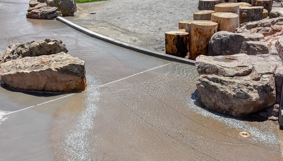 View of natural boulders and lithocrete with running water in a stream bed on a hot day installed by Colorado Hardscapes.