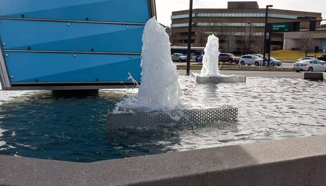 Up-close photo of Denver Tech Center water feature with three geyser nozzles and a large prism centerpiece.